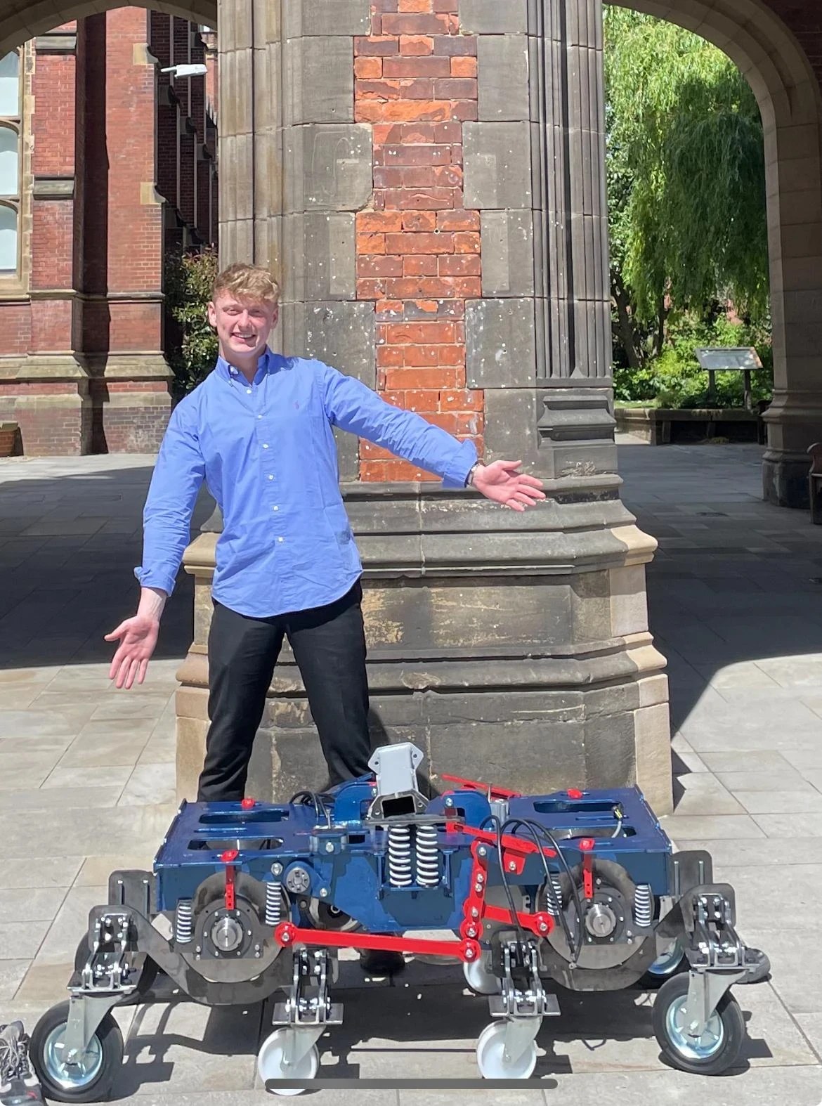 David Stewart standing behind the completed bogie and unsprung assembly, the blue chassis with red anti-roll bar and steering links visible